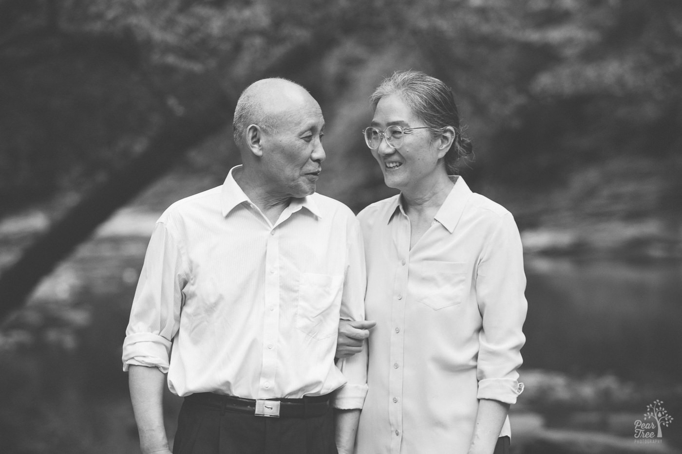 Smiling Chinese woman holding her husband close by his arm.