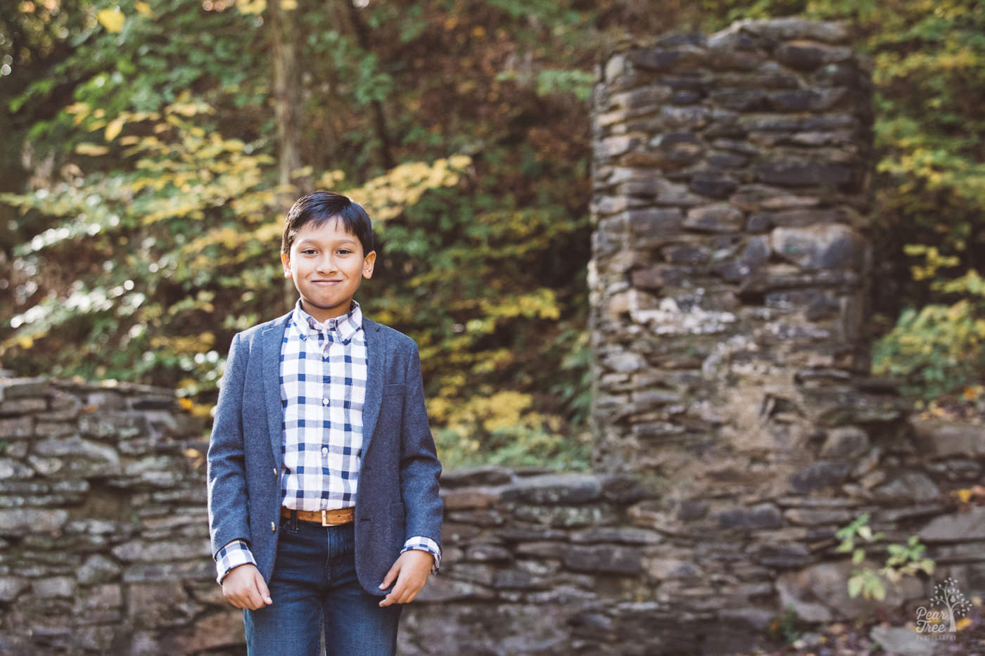 Young boy in blue blazer and jeans, standing and smiling in Sope Creek mill ruins.