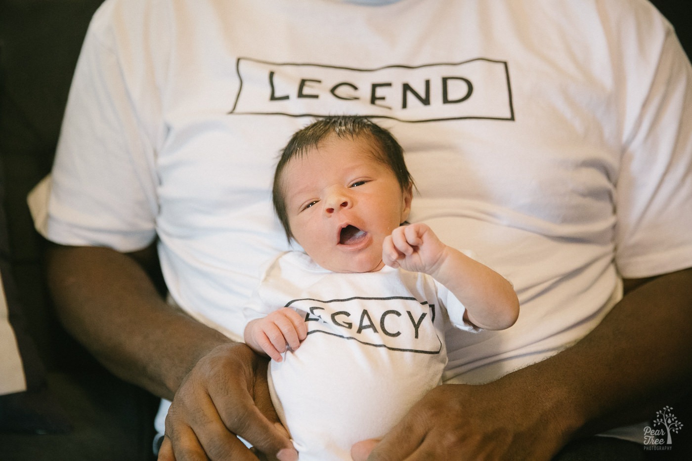 Dad in LEGEND t-shirt holding his five day old son wearing a LEGACY onesie.