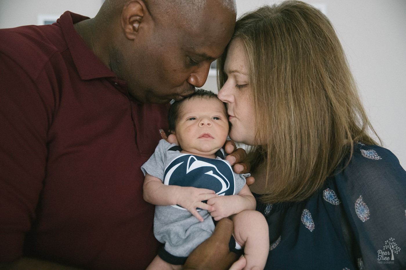 Inter-racial parents holding and kissing their five day old baby boy during their legacy lifestyle newborn session.