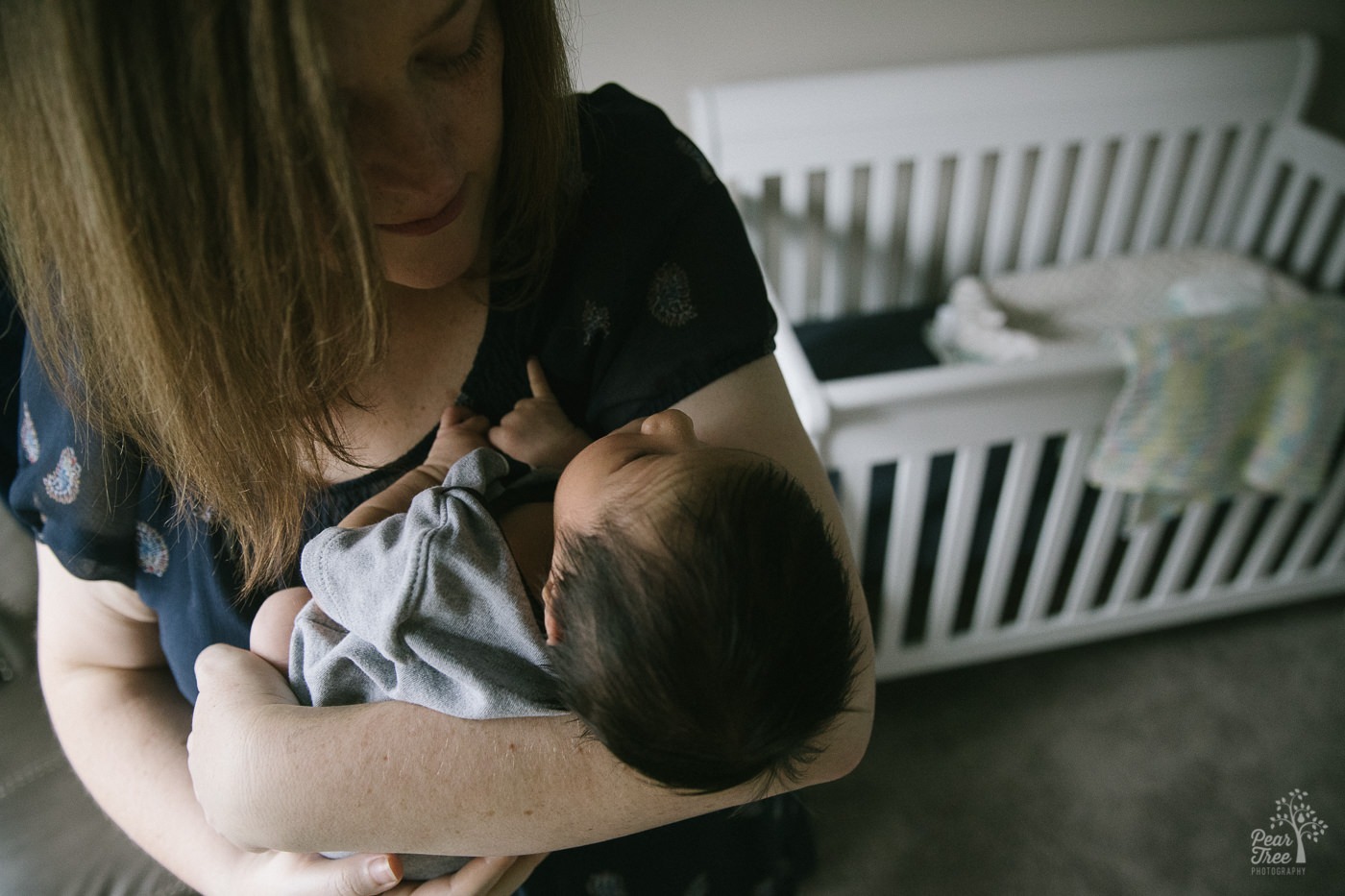 New mom holding her newborn baby boy while swaying in front of his crib.