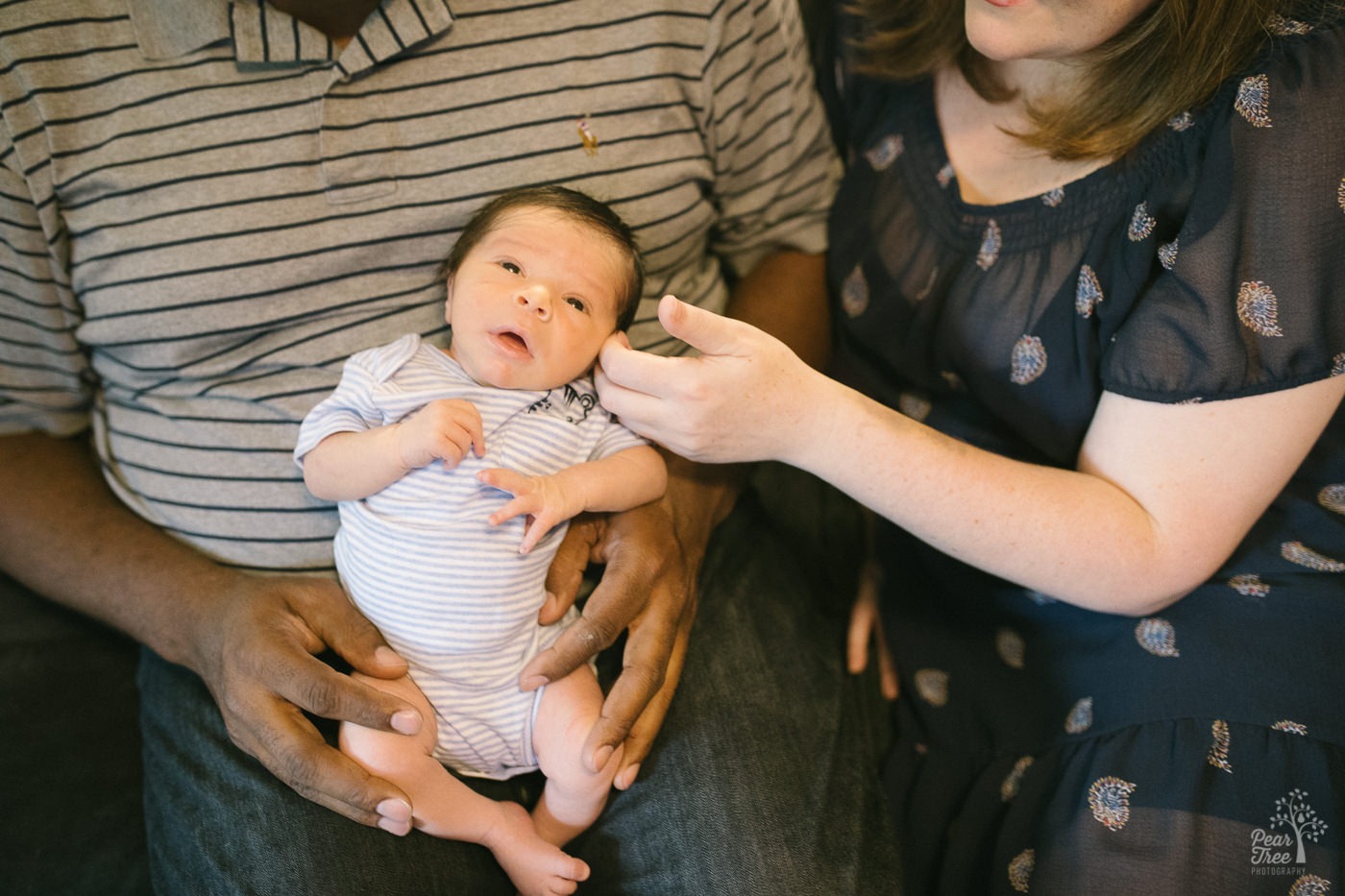 Inter-racial parents holding their five day old son and stroking his cheek during their lifestyle newborn session.