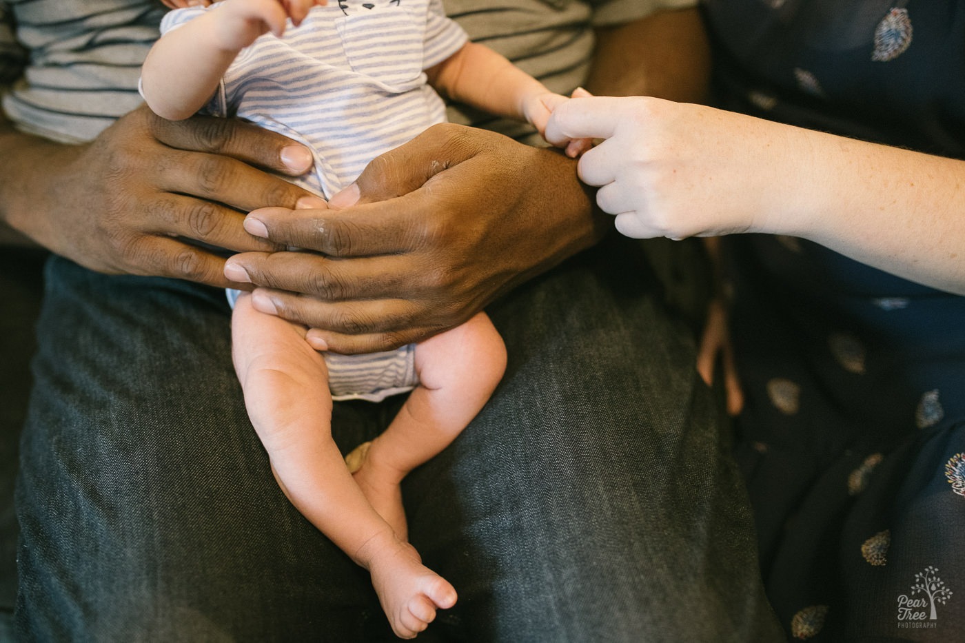 Inter-racial parent hands holding five day old newborn baby boy by his hand and around his belly.