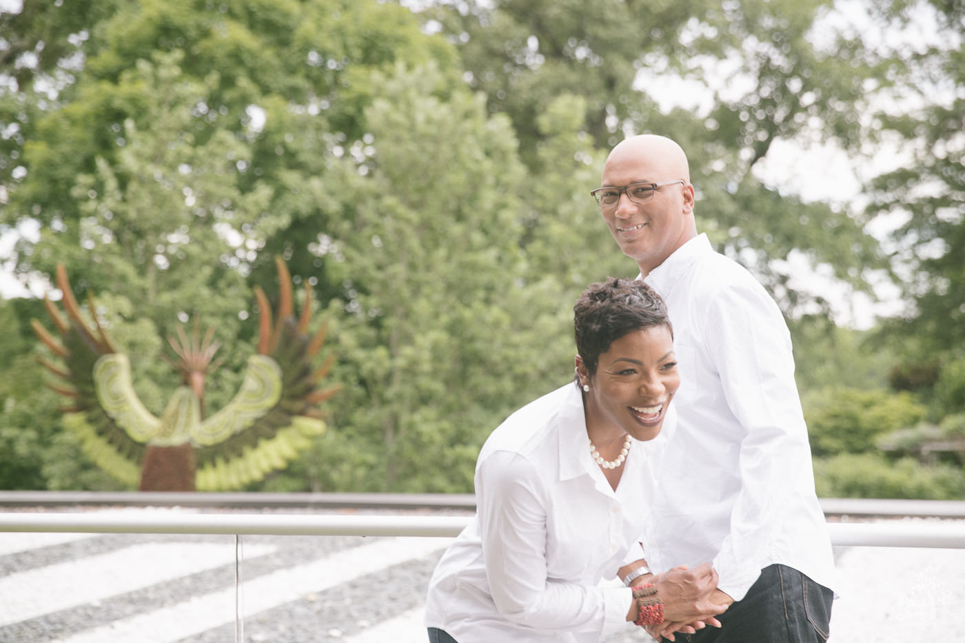 Engaged couple laughing in front of Atlanta Botanical Garden phoenix with raised wings