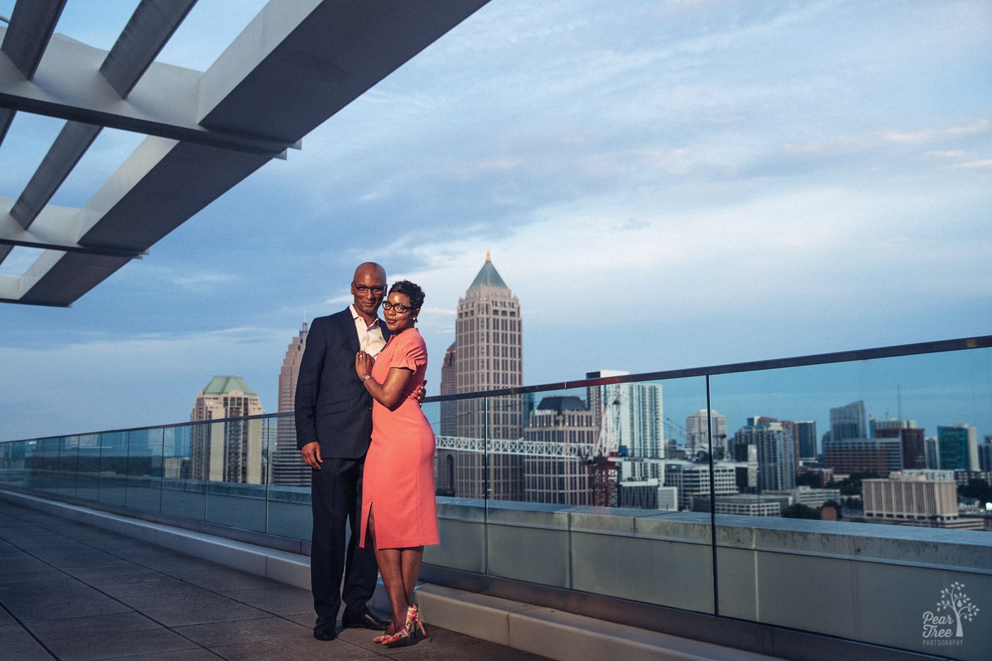 Striking couple in fancy dress on Atlantic Station 18th floor balcony with midtown Atlanta skyline in background during their engagement session