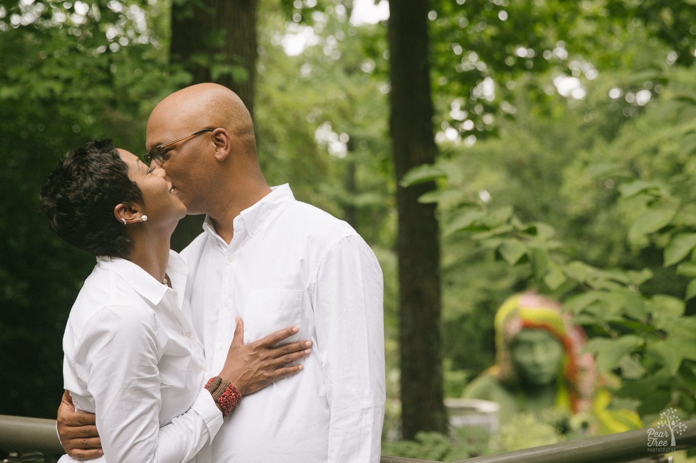 Happy African American couple hugging and whispering into each other's ears in front of the Atlanta Botanical Garden Earth Goddess