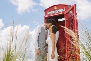 Gorgeous bride + groom kissing in front of red telephone booth with Just Married sign and blue skies for their destination wedding