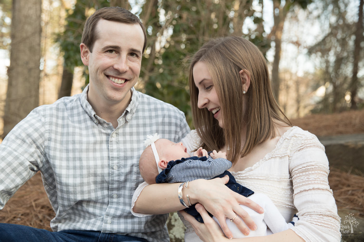 Smiling, happy parents holding their newborn daughter in downtown Woodstock park.