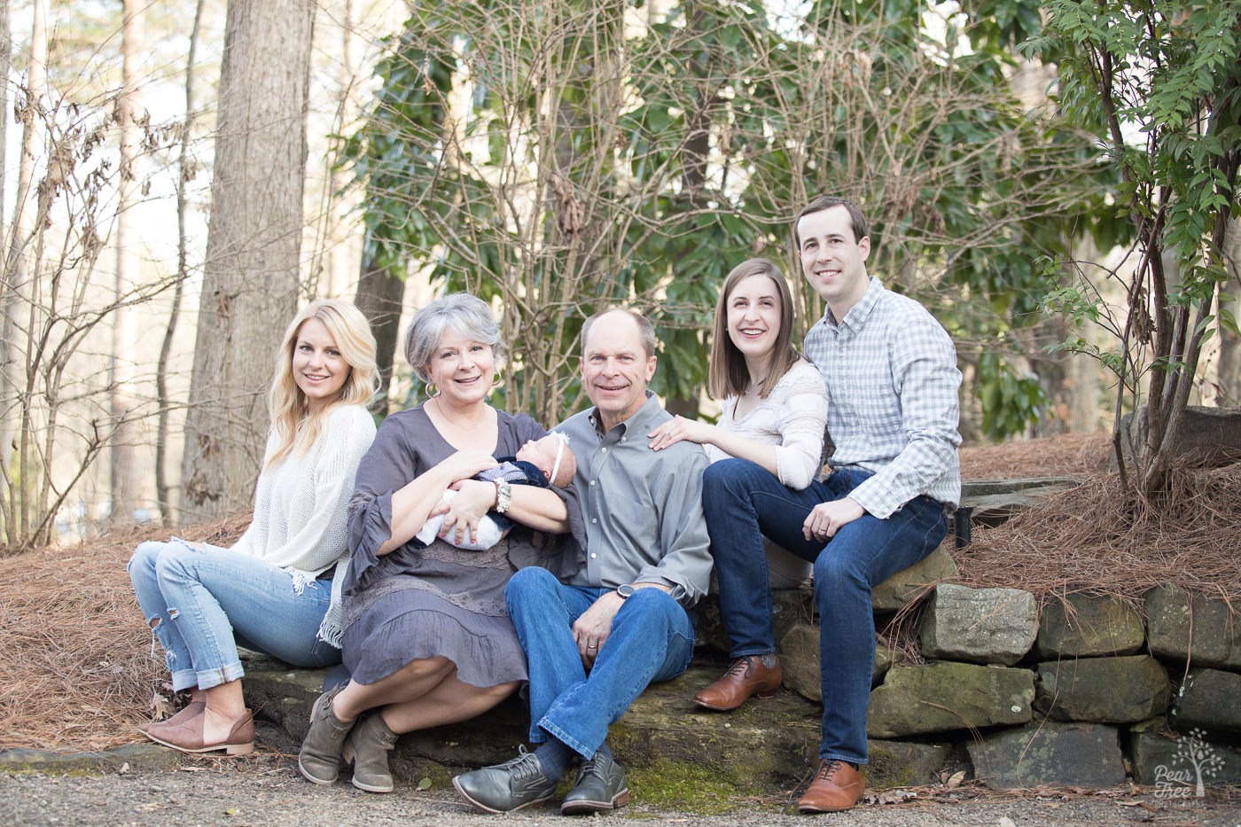 Three generations of happy family members sitting together with their newborn baby in downtown Woodstock park.