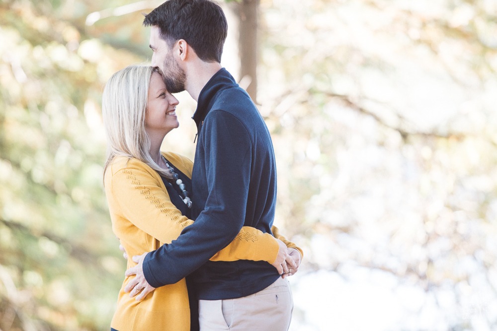 Romantic husband and wife holding each other close laughing while he kisses her on the forehead.