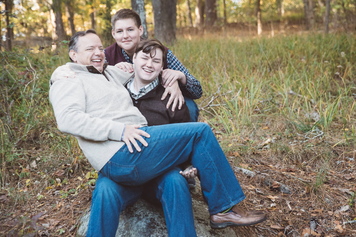 Dad sitting on his oldest teenage sons lap and laughing.