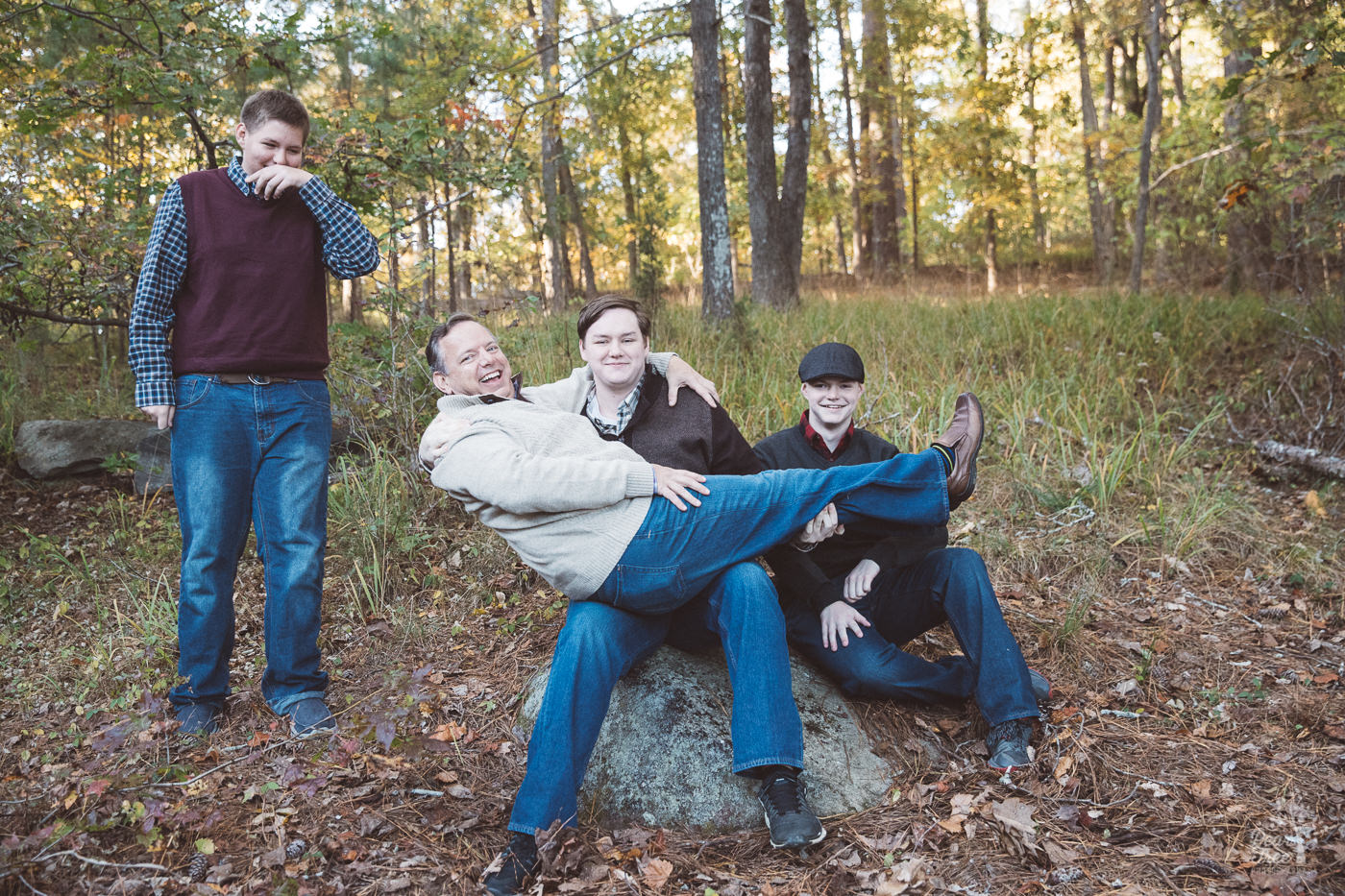 Dad laying on oldest teenage son's lap while other two sons crack up.