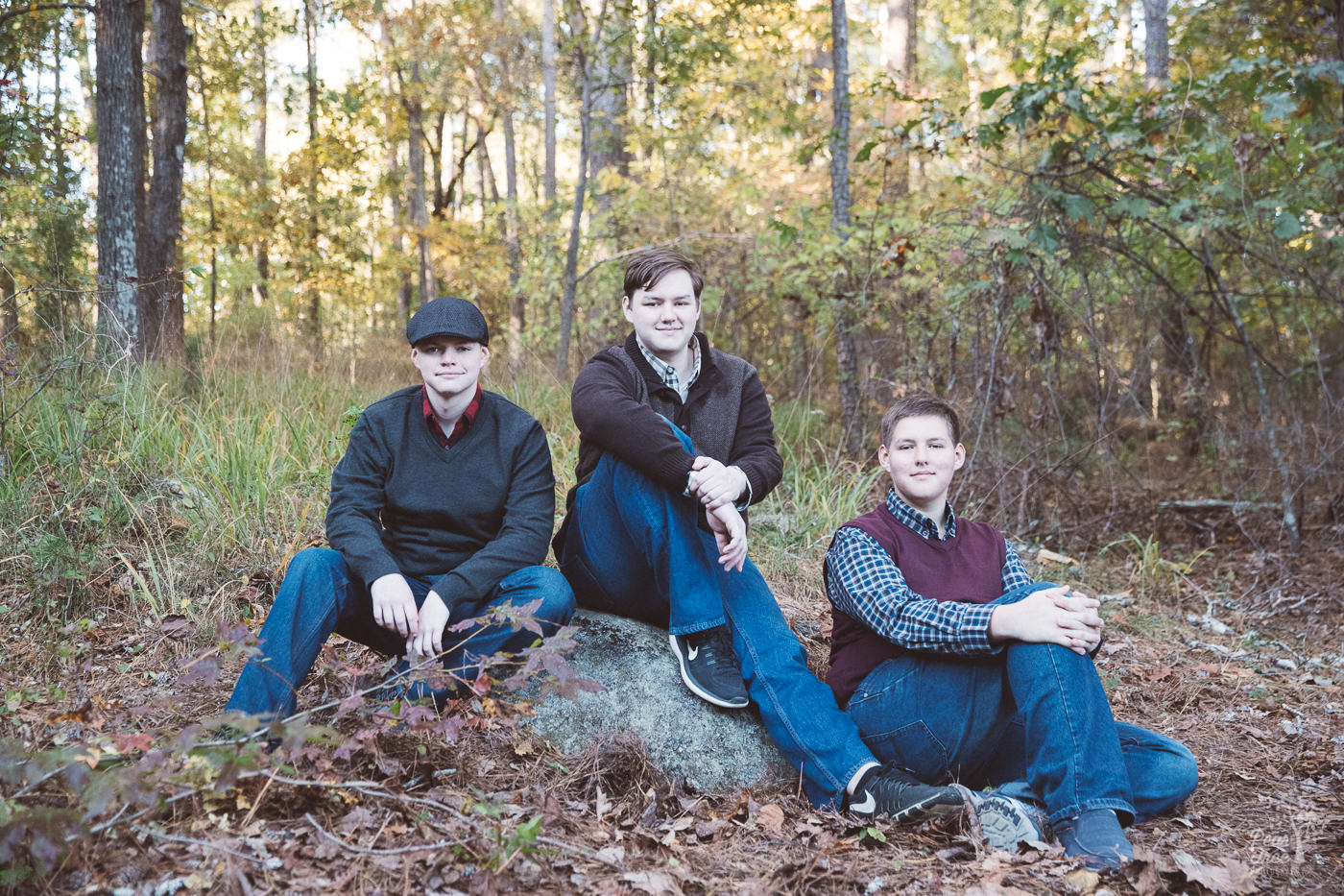 Three teenage brothers sitting in Stone Mountain woods smiling and trying to be serious.