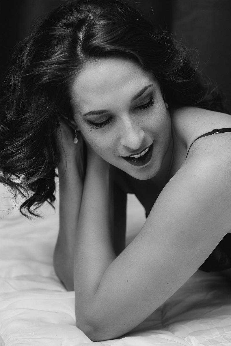 Black + white boudoir image of gorgeous brunette woman with curly hair look down and smiling