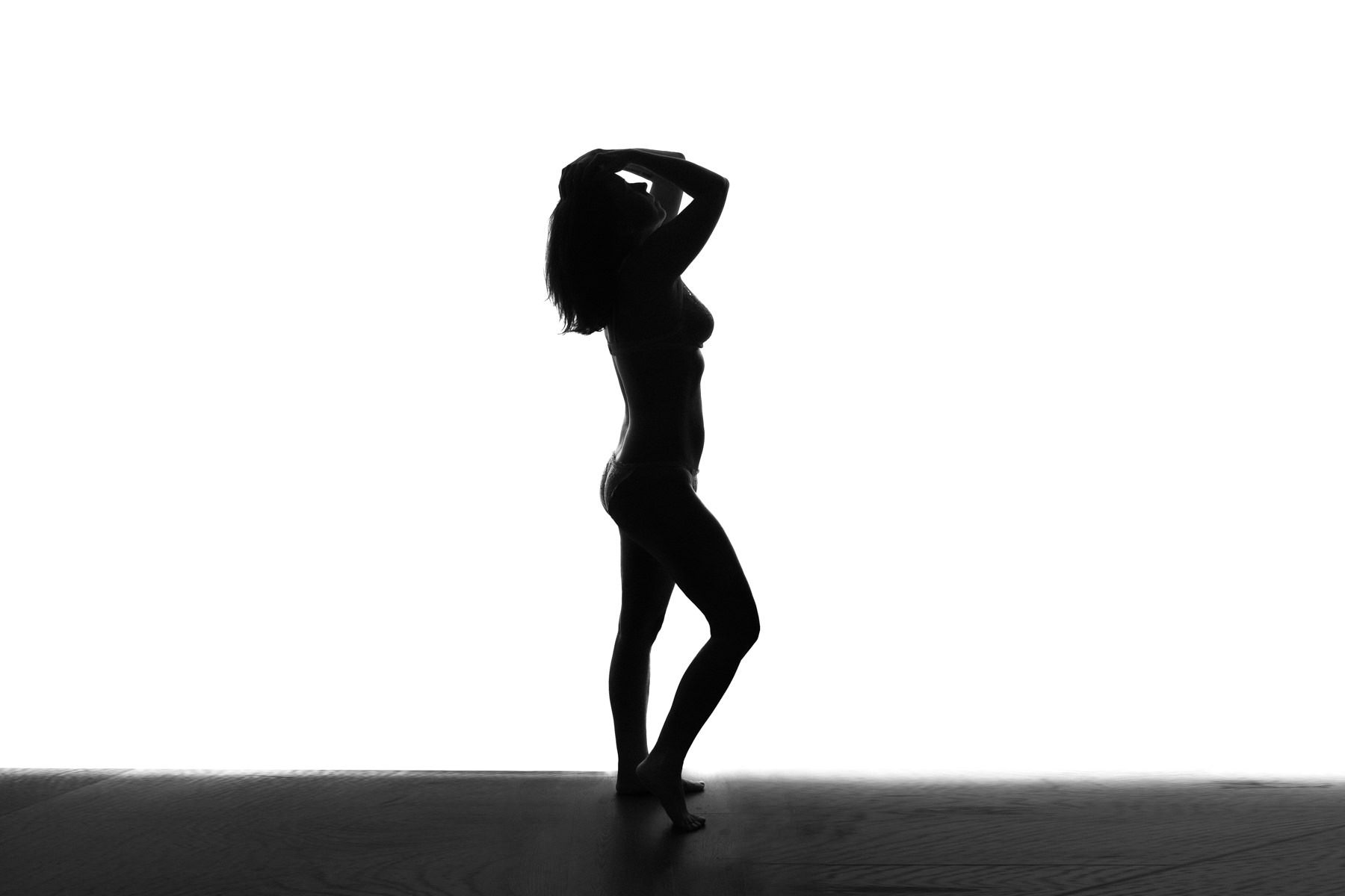 Silhouette of woman in lingerie with one knee bent and arms reaching upwards