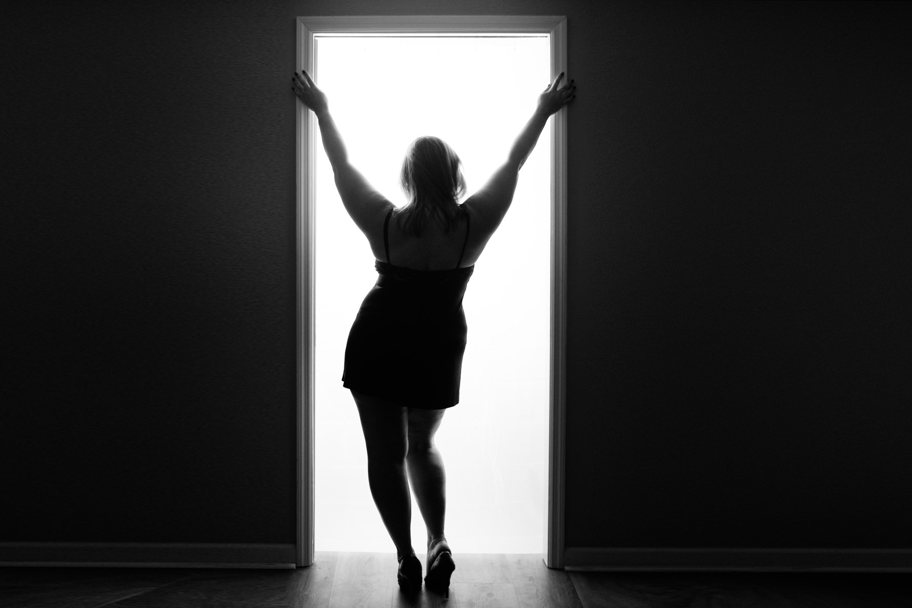 Curvy woman standing in a doorway with hip kicked to the side and arms outstretched above her