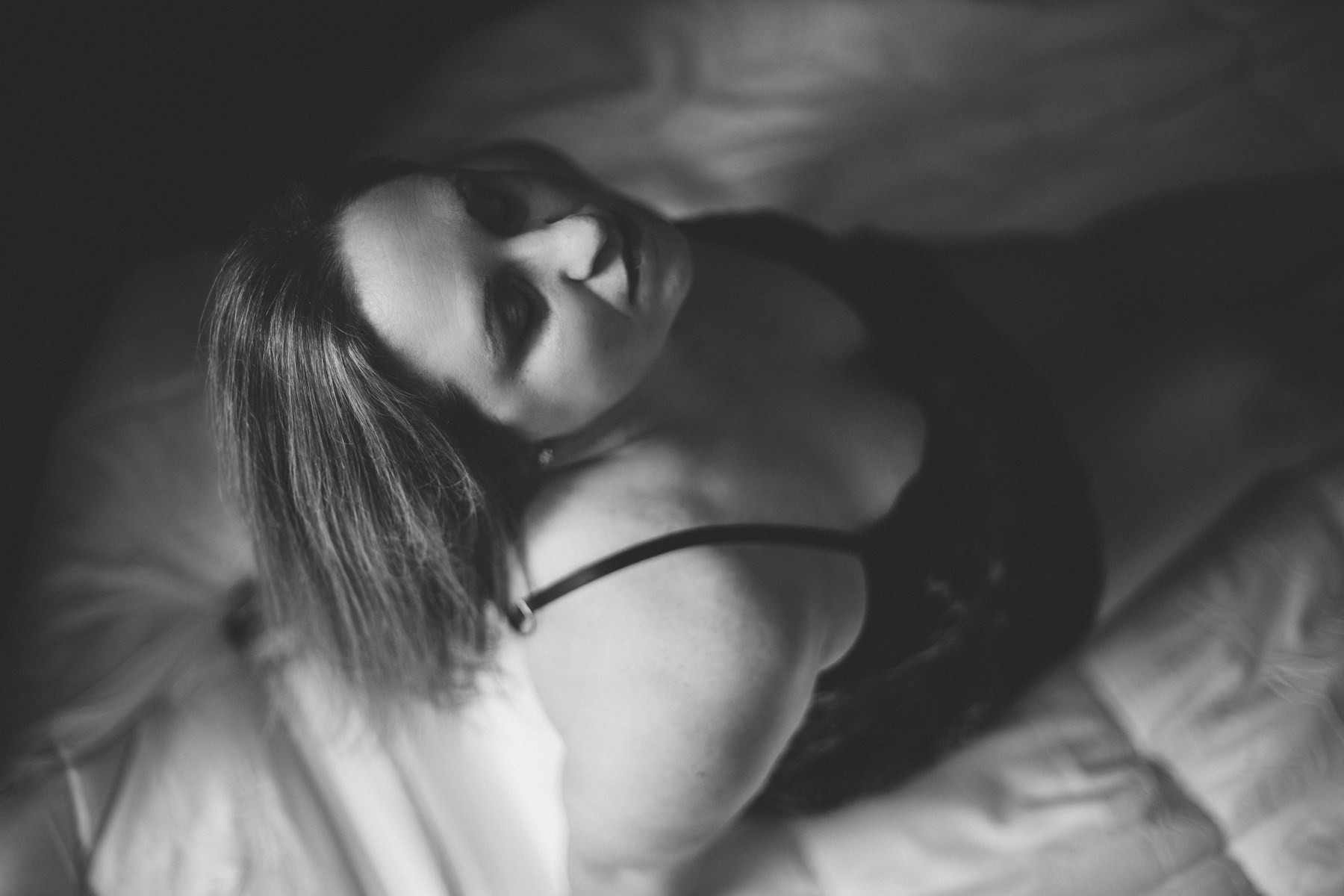 Black and white boudoir photo of a woman sitting back and hit tilted up