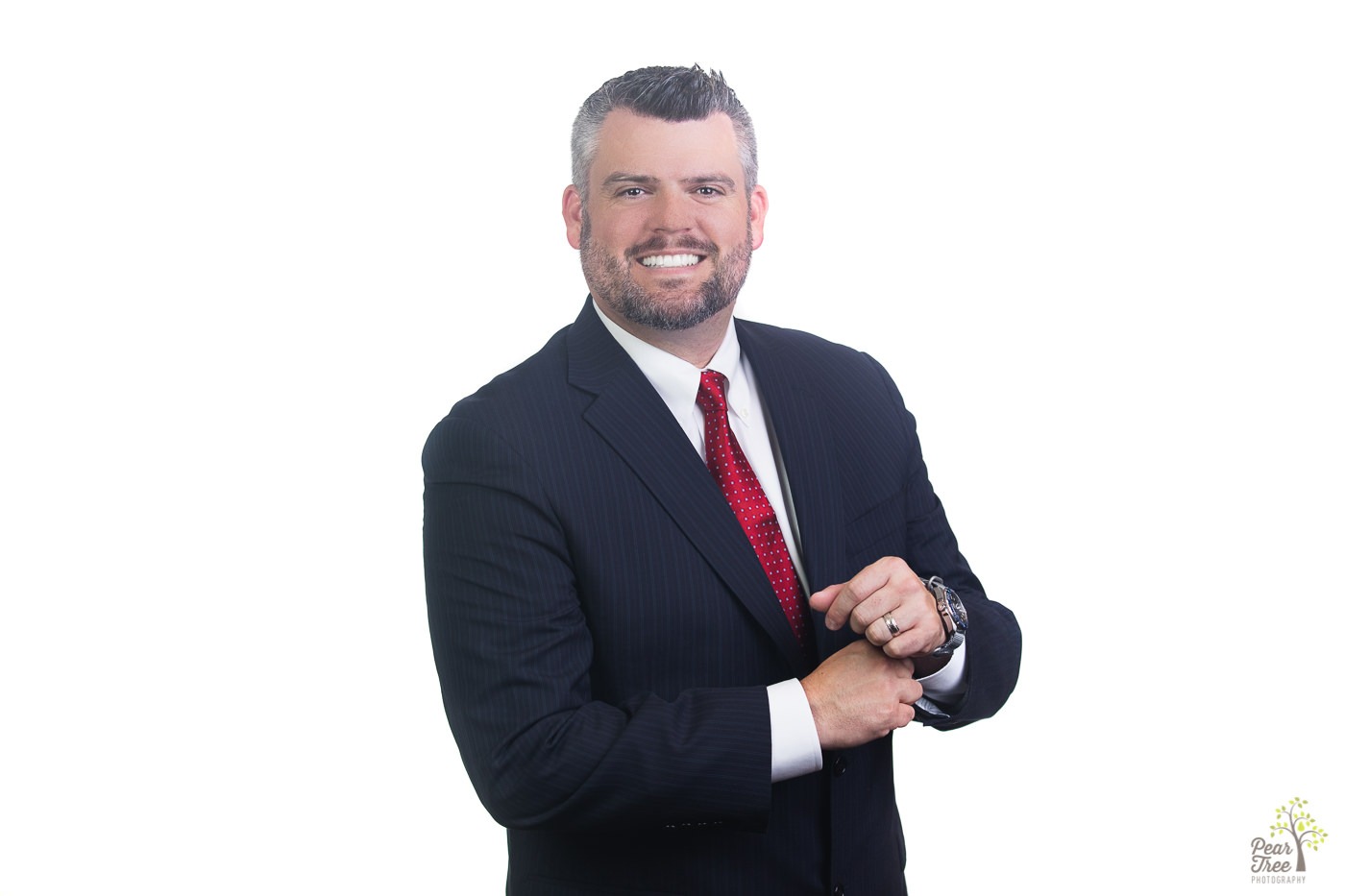 Professional headshots in Canton making with a man standing in a dark suit and a red tie adjusting his sleeve