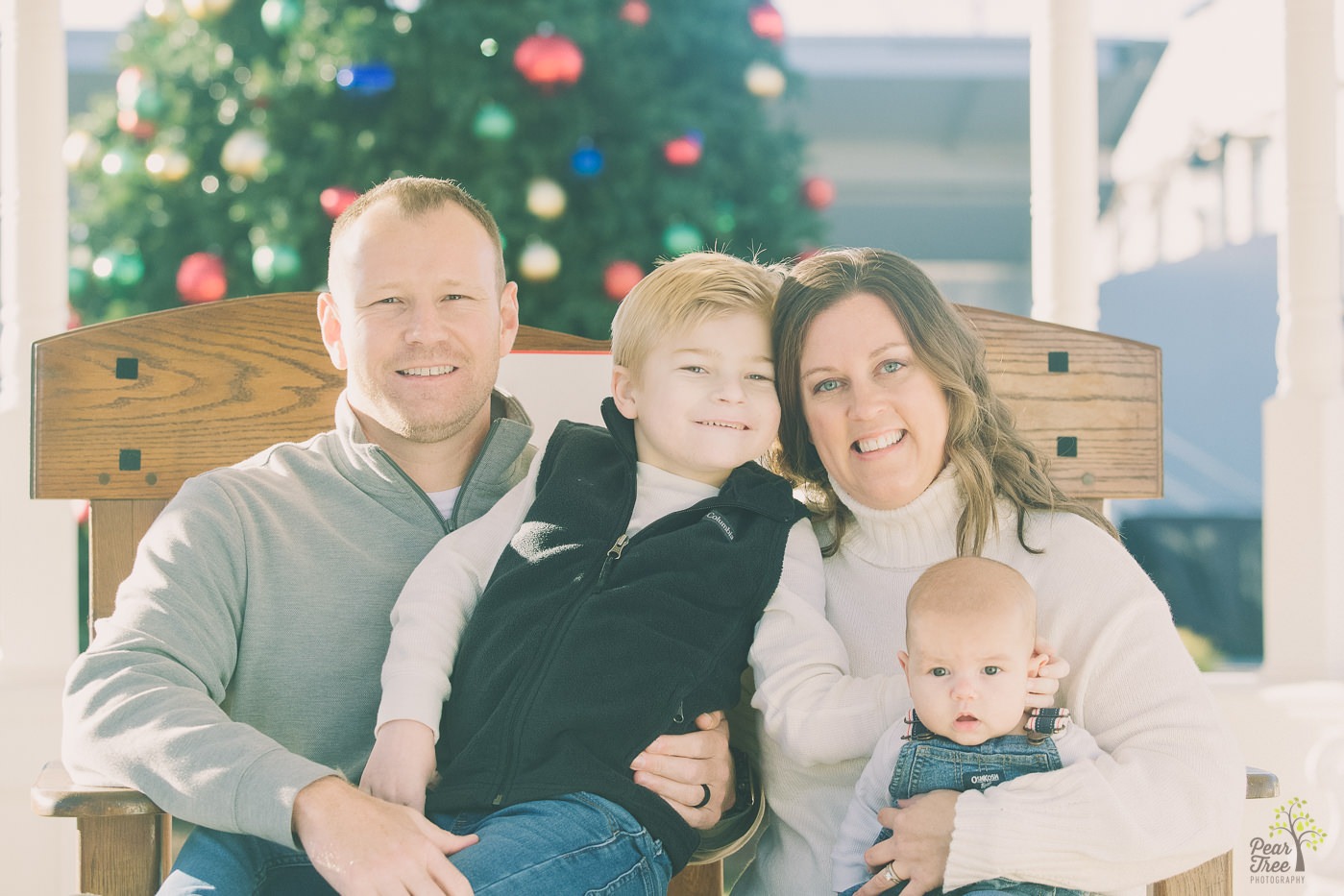 Cute family of four snuggled on a bench in front of a Christmas tree in downtown Canton