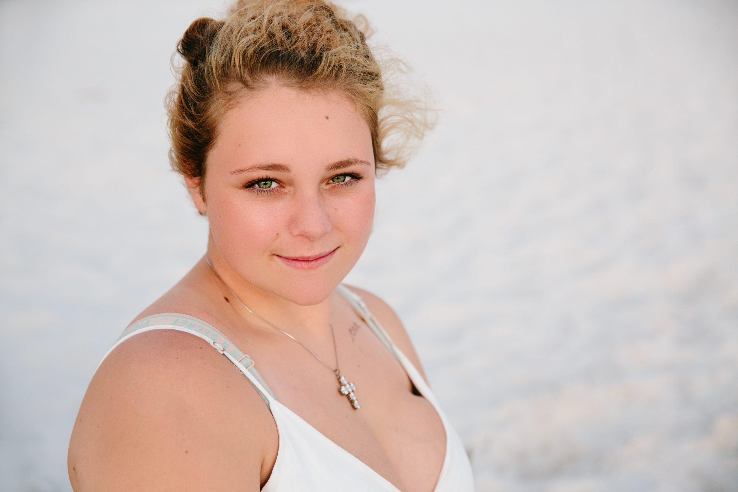 Beautiful high school senior girl with curly hair smiling on the beach