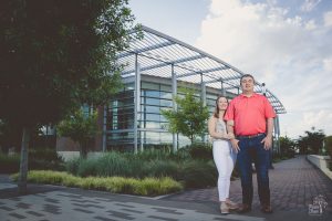 Husband and wife standing smiling in front of City Springs building with blue sky and clouds
