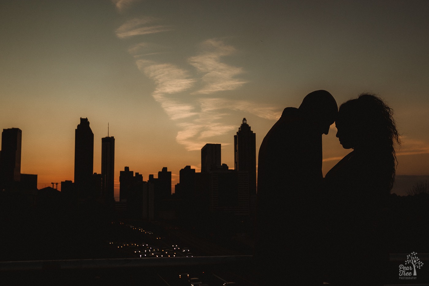 African American couple standing in silhouette with foreheads touching at sunset on Jackson Street Bridge.