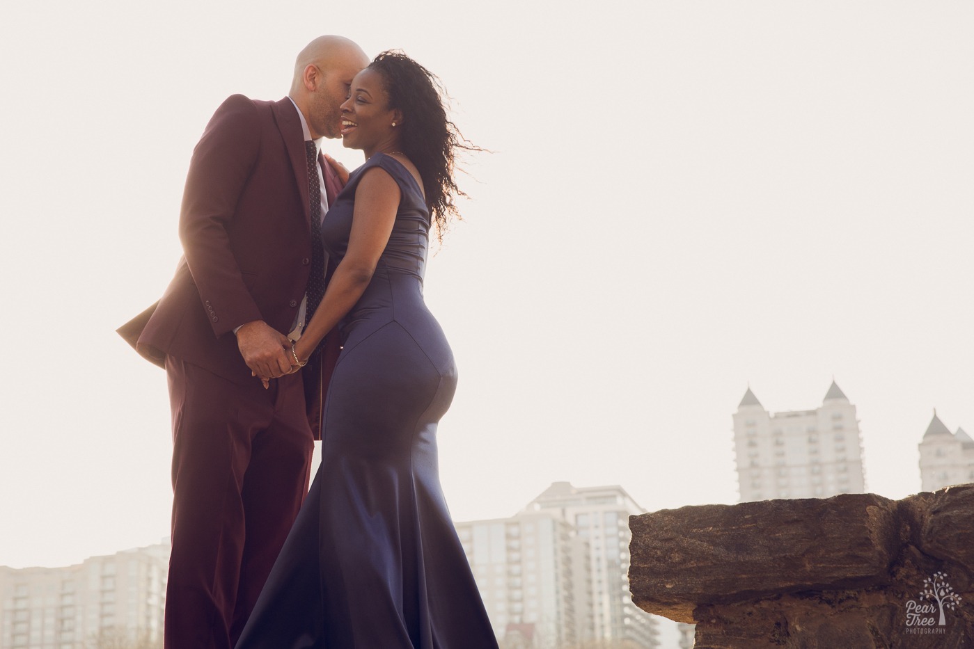 African American couple holding hands while the husband whispers in her ear and she laughs. Atlanta skyline behind them.