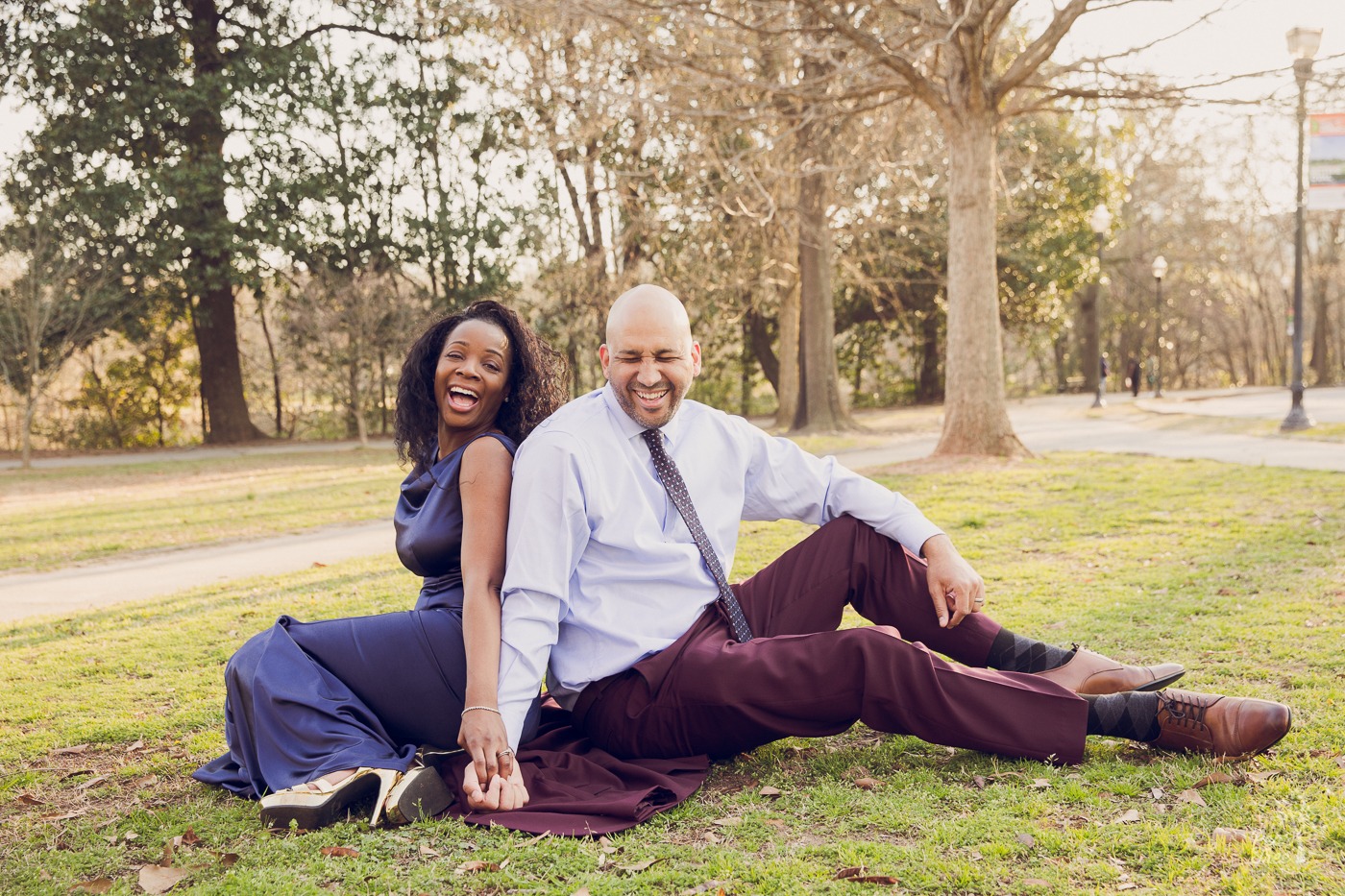 African American couple holding hands while sitting on the ground in Piedmont Park while laughing hard.