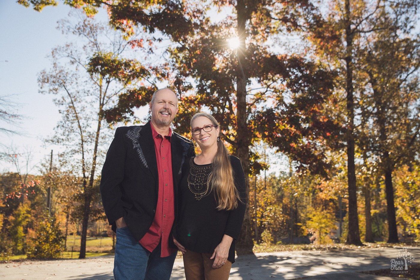 Branding image of man wearing a red shirt and black blazer next to his smiling wife with a long pony tail