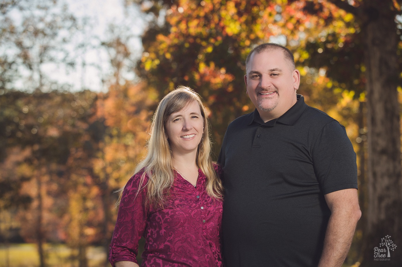 Man in black shirt smiling next to his blond wife in a magenta shirt