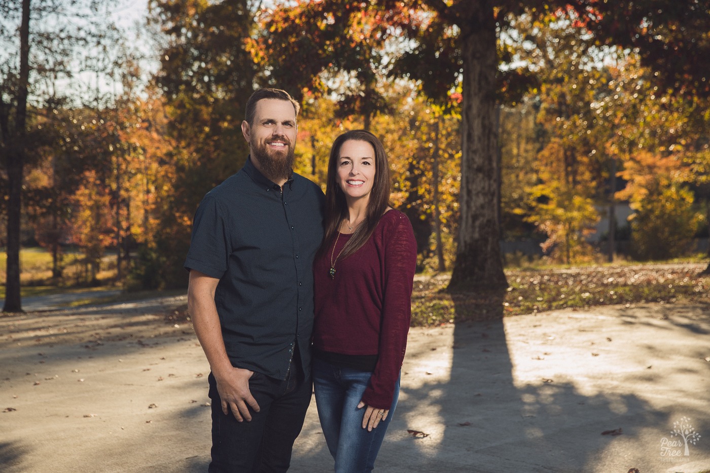Smiling husband and wife standing in front of fall trees