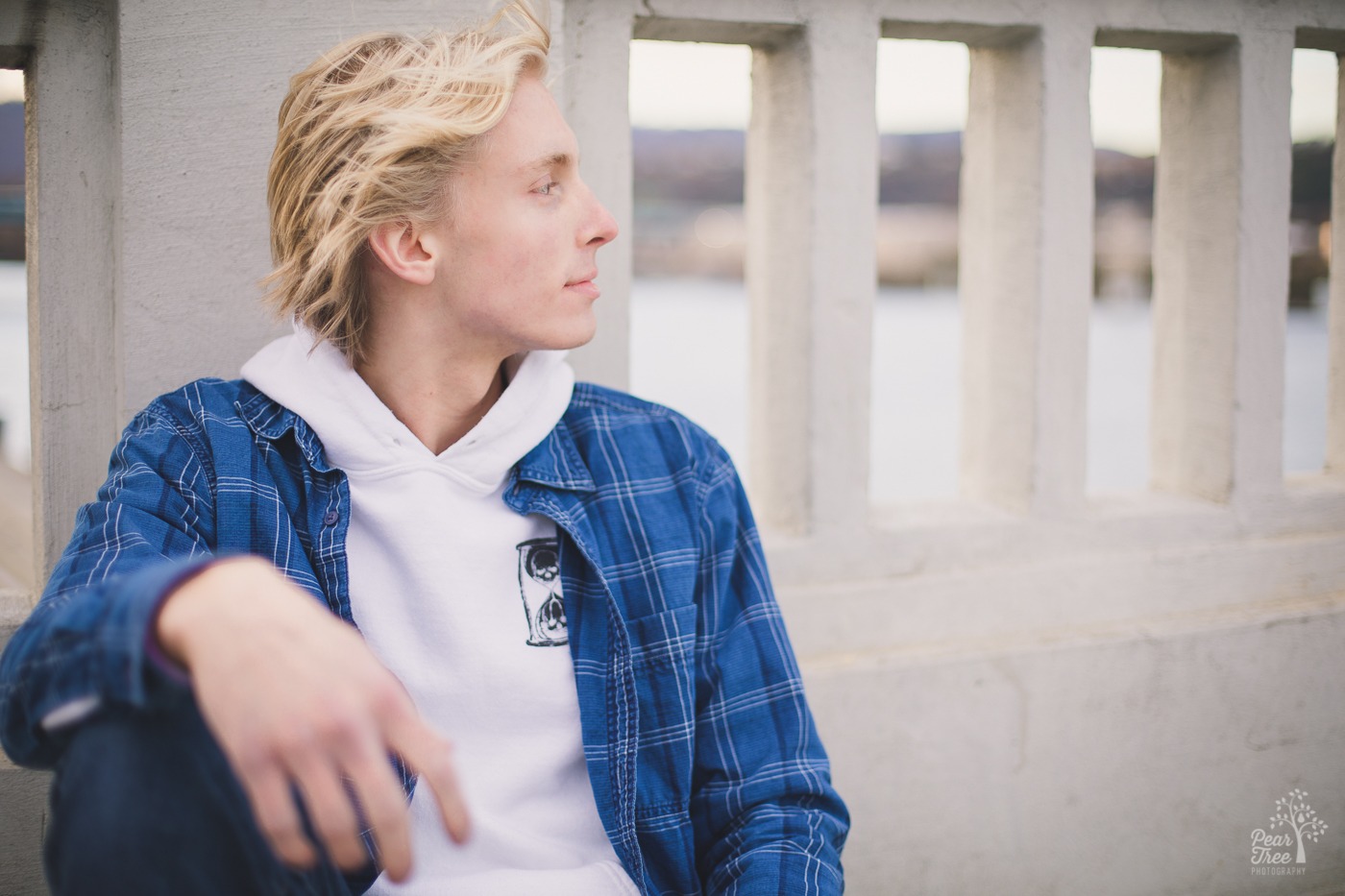 Blond man sitting on white bridge over a river looking to the side