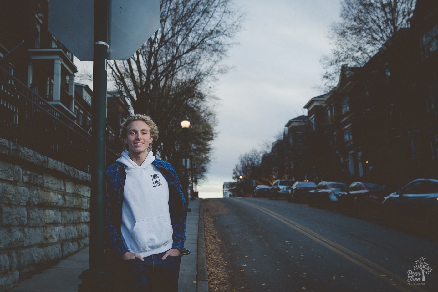 Senior boy leaning against a stop sign on a residential Chattanooga street corner with his hands in his jeans pockets smiling