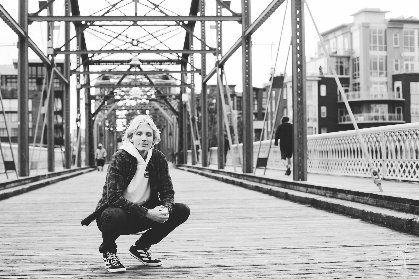 Black and white photograph of a high school senior boy squatting in the middle of Chattanooga bridge