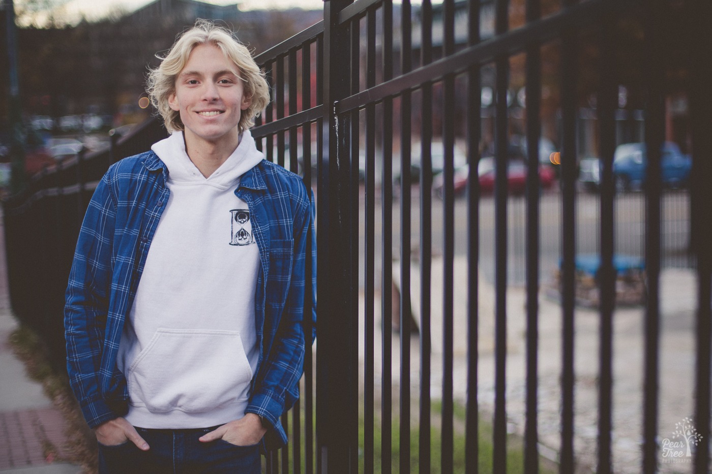 Smiling blond man with hands in pockets while leaning against a black metal fence