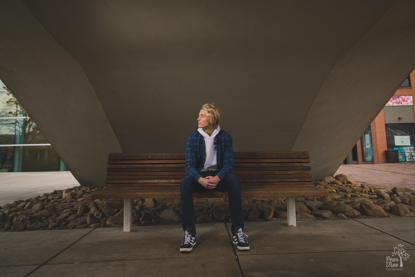 Blond high school senior boy in blue sitting on a wooden bench under a bridge outside of the Tennessee Aquarium