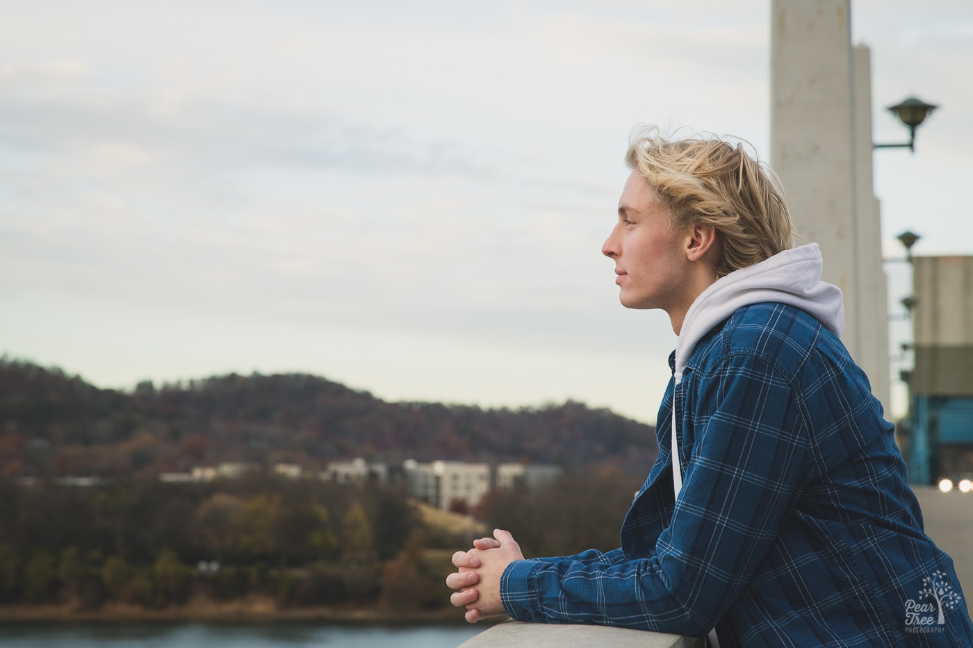 Blond man in white hoodie and blue flannel shirt standing on bridge over the Tennessee River