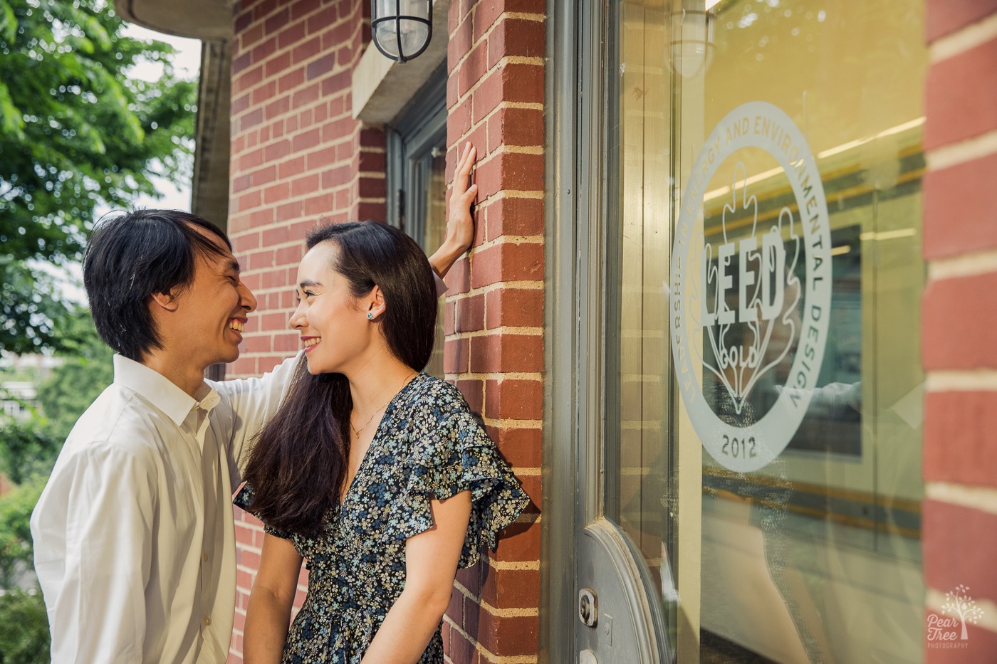 Laughing Asian-American during their engagement photography session outside of a brick building