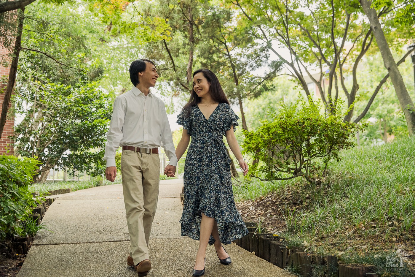 Happy engaged couple holding hands as they walk down a curvy path underneath a dream cover of trees.