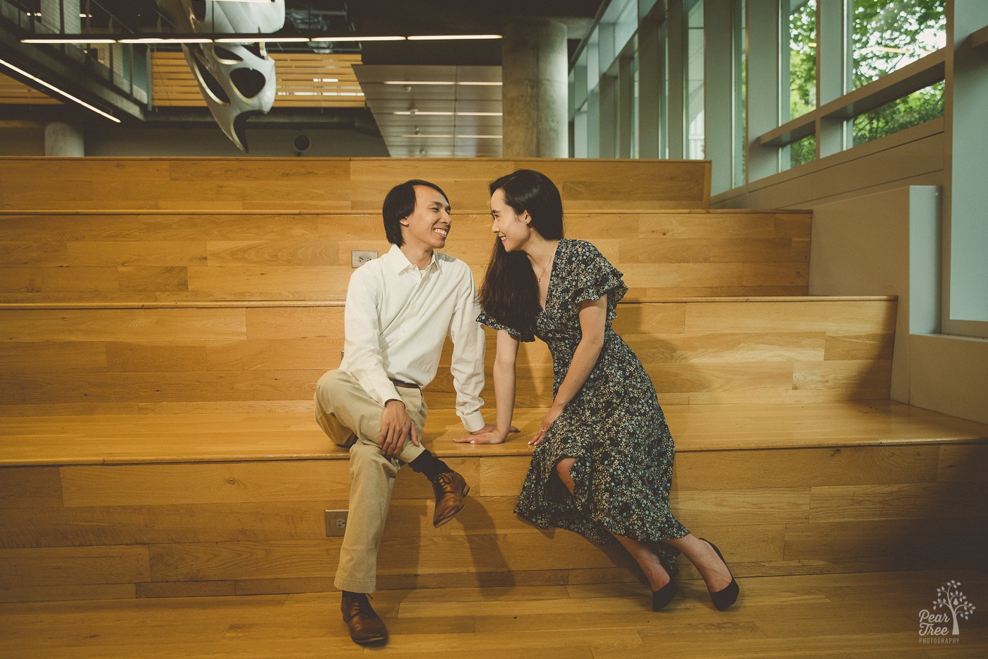 Happy couple leaning in close while smiling and sitting on tall wooden steps inside Georgia Tech