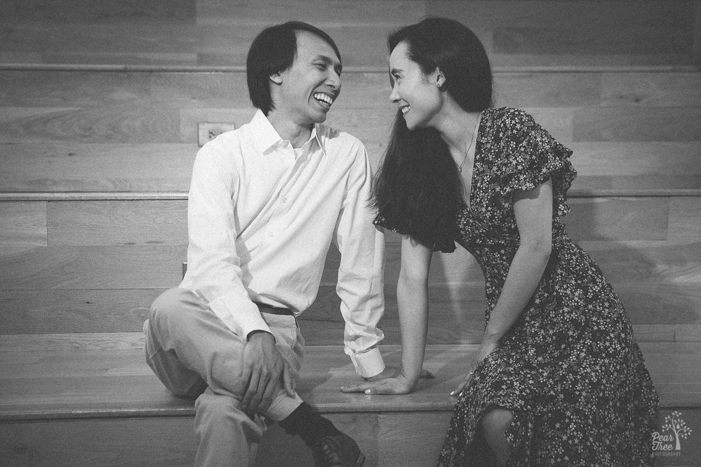Laughing Asian-American couple sitting close together in black and white photograph