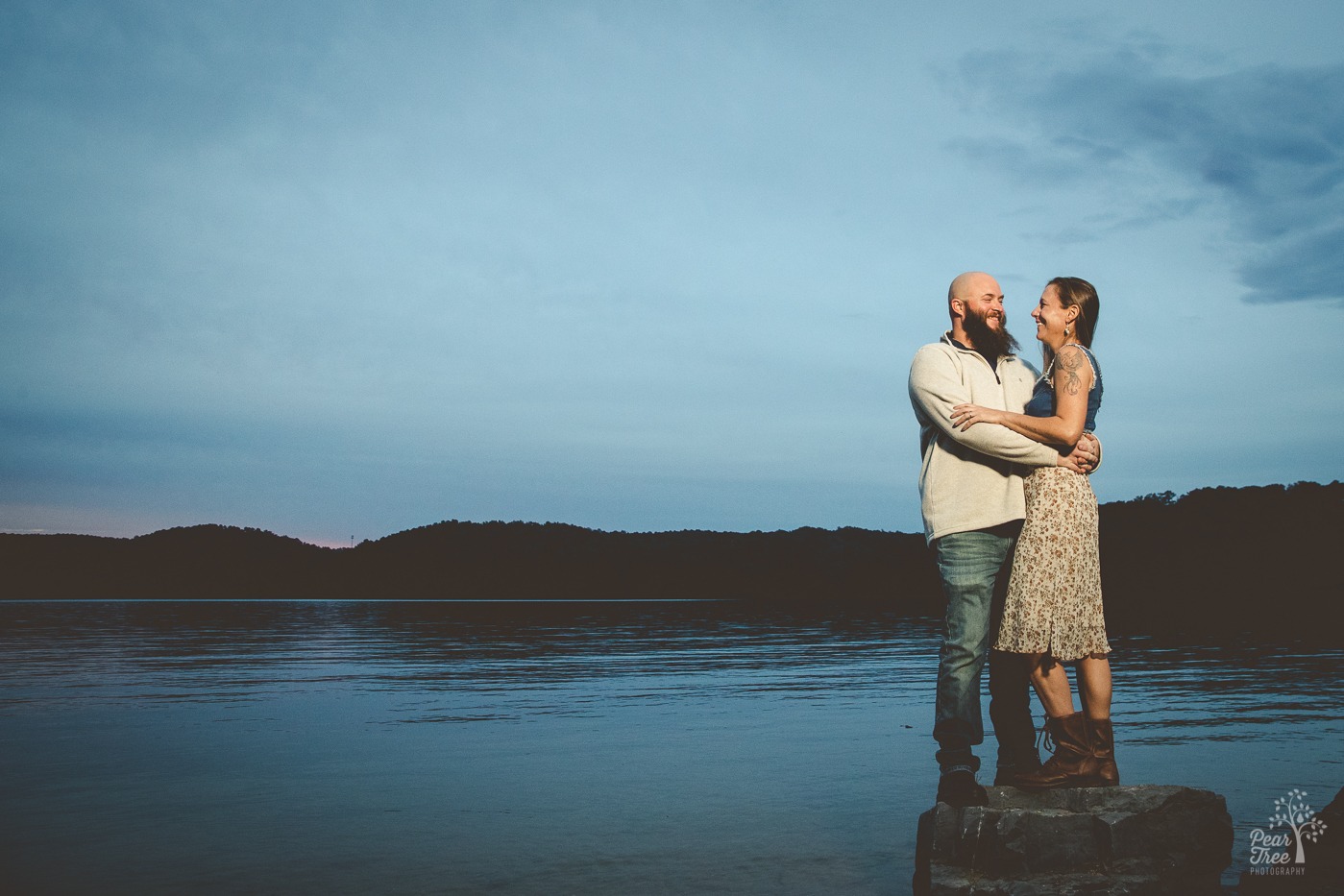 Smiling couple holding each other close while standing in front of Lake Arrowhead at dusk