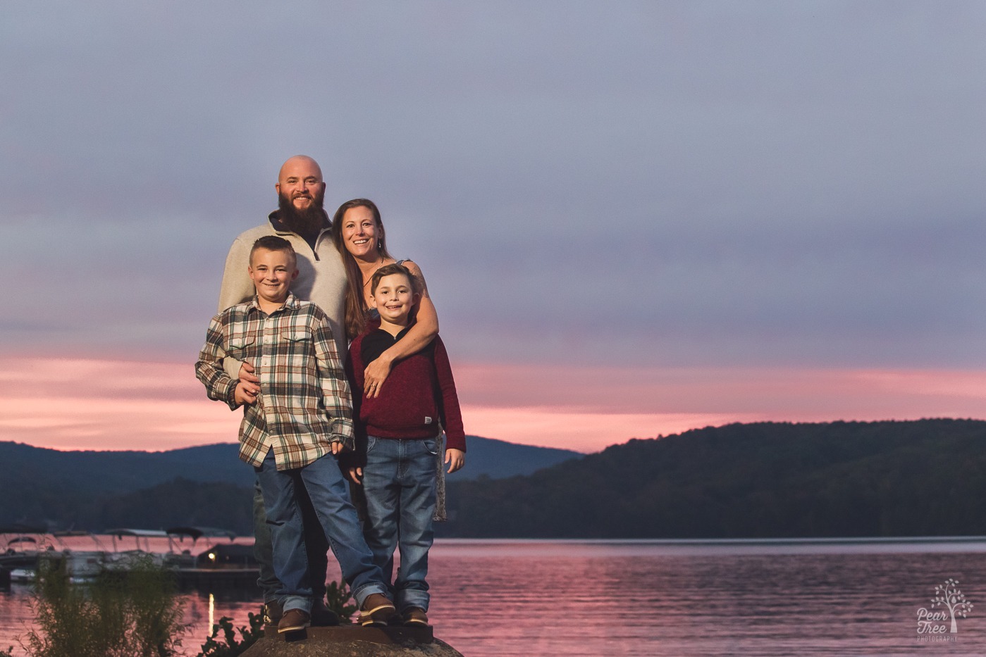 Family of four huddled close in front of Lake Arrowhead at sunset