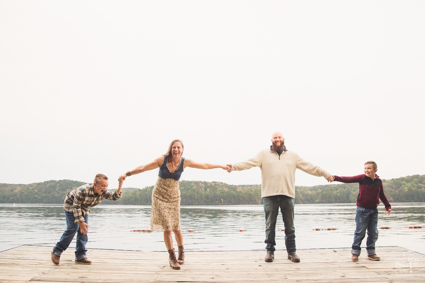 Laughing family of four holding hands and stretched out as far as possible from each other on Lake Arrowhead dock.