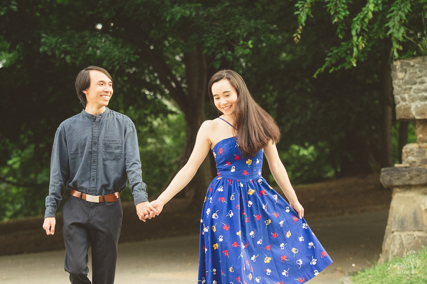 Happy Asian-American couple holding hands while walking through Piedmont Park during their engagement photography session