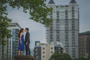 Engaged Chinese-American woman in a blue dress nuzzling noses with her Vietnamese-American fiance at Piedmont Park with Atlanta skyline behind them