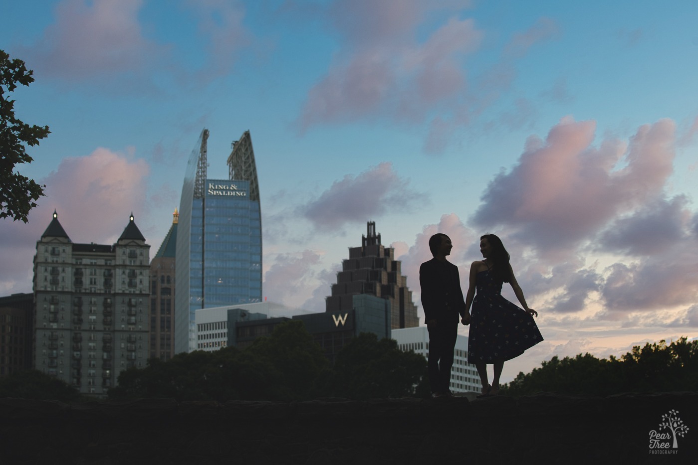 Silhouette of engaged couple holding hands in Atlanta skyline at sunset