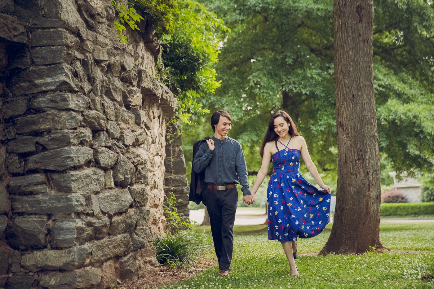 Loving engaged couple holding hands while walking next to Piedmont Park stone wall