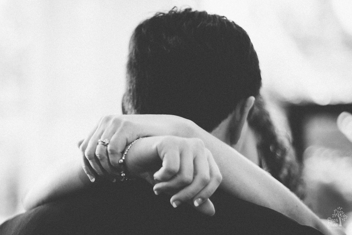 Black and white photograph of bride's hands criss crossed behind her husband's neck and over his shoulders.