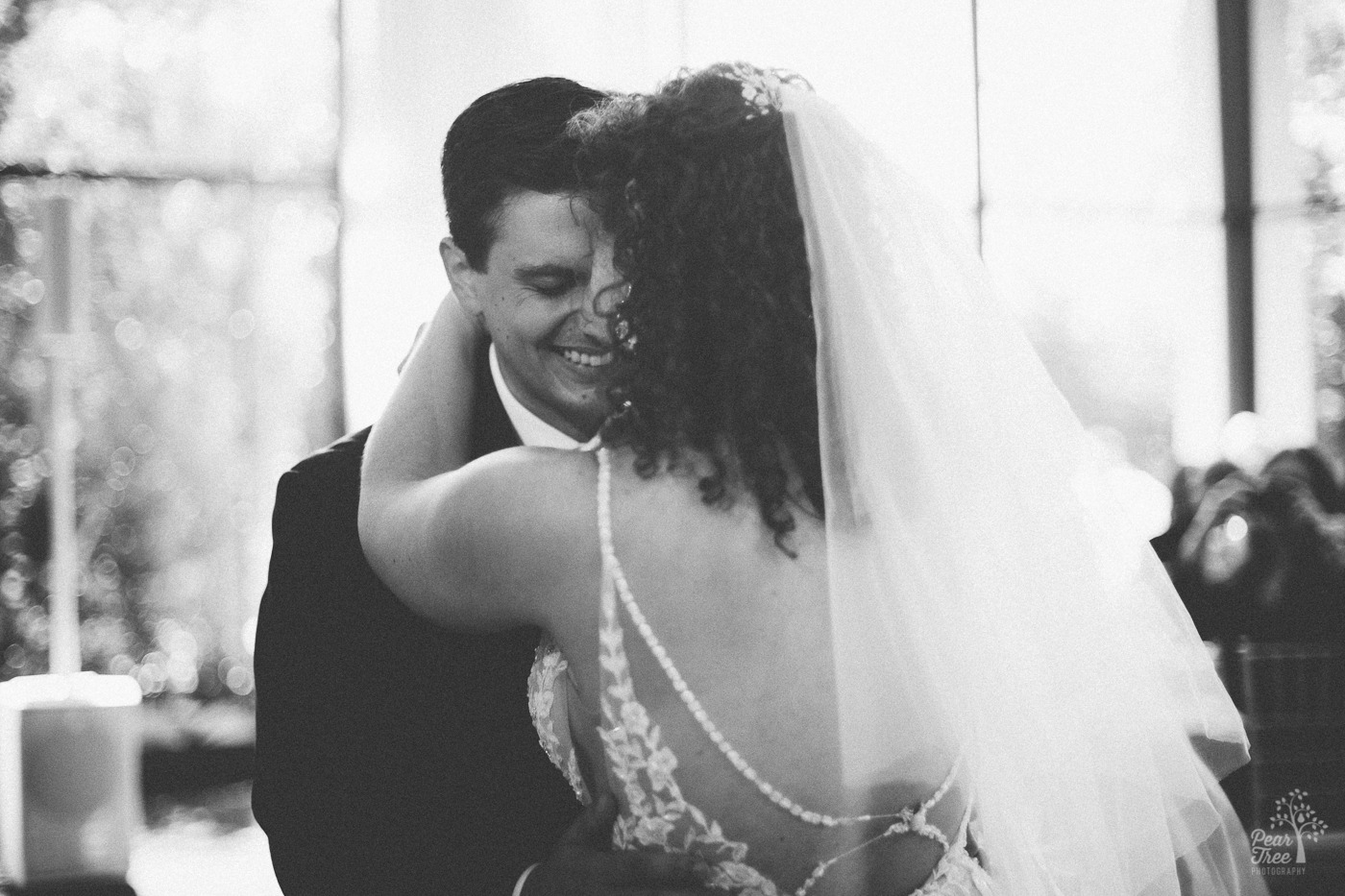 Black and white photograph of groom smiling over his bride's shoulder as they dance at The Atrium